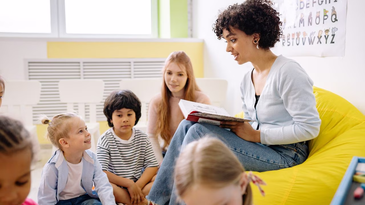 Teacher sitting in a yellow bean bag chair reading to a group of students