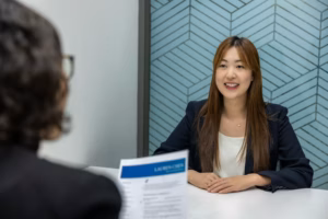 Two women seated at a table for an interview, viewed from over the shoulder of the interviewer